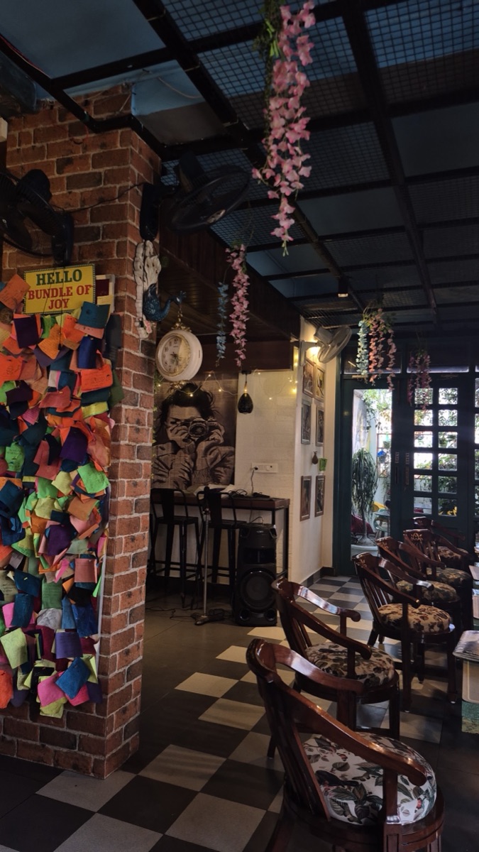 Brick pillar, the colourful notes wall and cane chairs on a checkered floor inside Magpie Cafe
